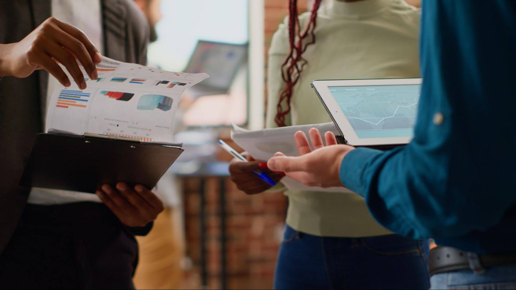 Three people using iPads and looking at charts printed on pieces of paper.